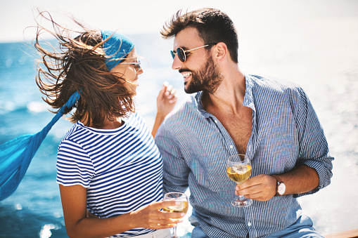 Young couple drinking white wine on the yacht and enjoying sailing.