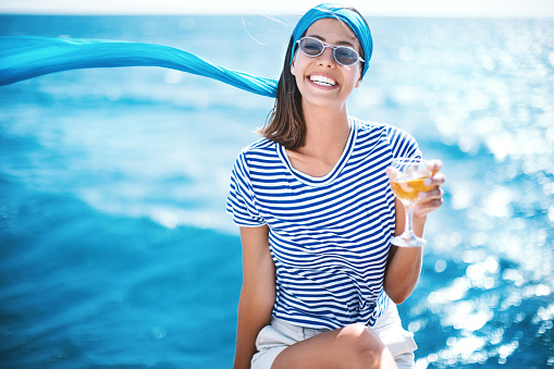 Young woman drinking white wine on the yacht, smiling and looking at camera.