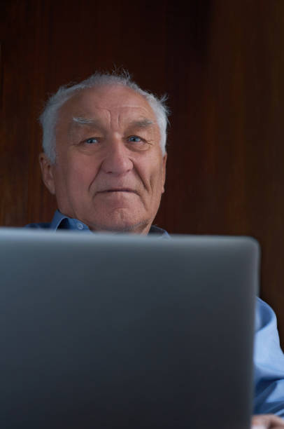 istock Senior grey-haired man using a laptop sitting in chair at home. 1093488640
