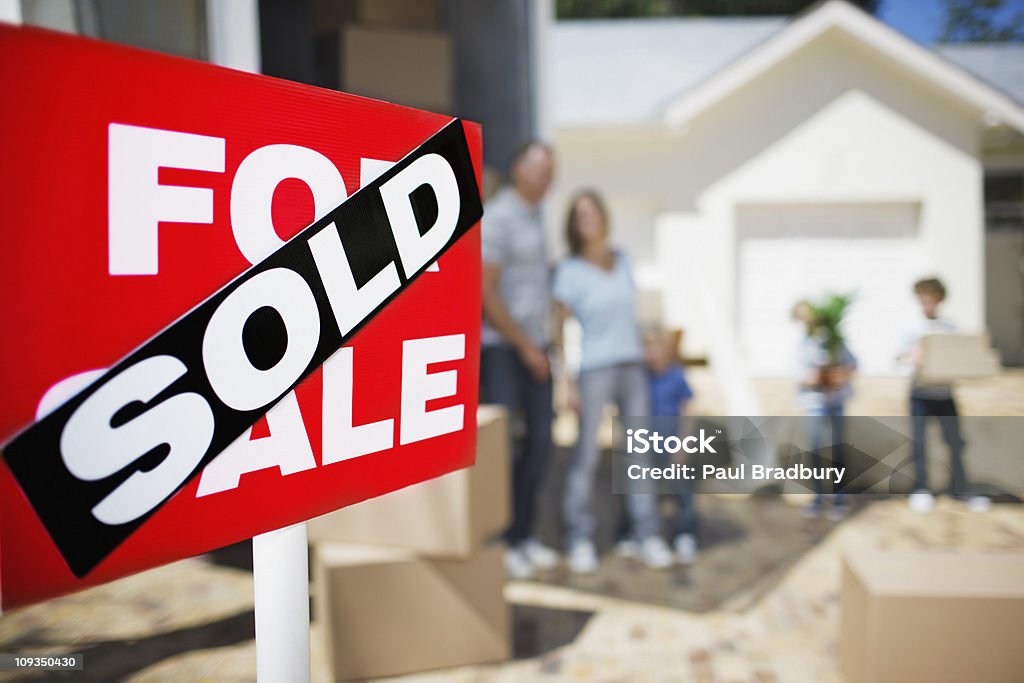 Verkauft-Schild auf Haus mit Familie im Hintergrund - Lizenzfrei Verkaufen Stock-Foto