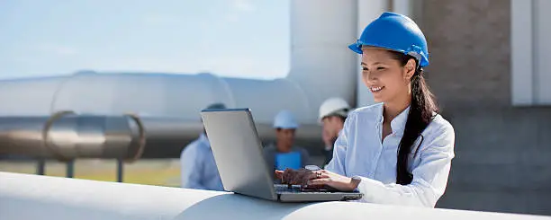 Photo of Businesswoman in hard-hat using laptop outdoors
