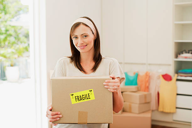 mulher de caixa de transporte com frágil autocolante na nova casa - cardboard box package box label imagens e fotografias de stock