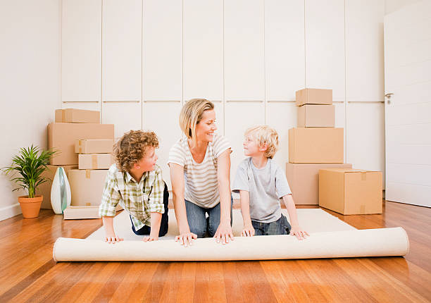 madre e figli unrolling tappeto in una nuova casa - unrolling foto e immagini stock