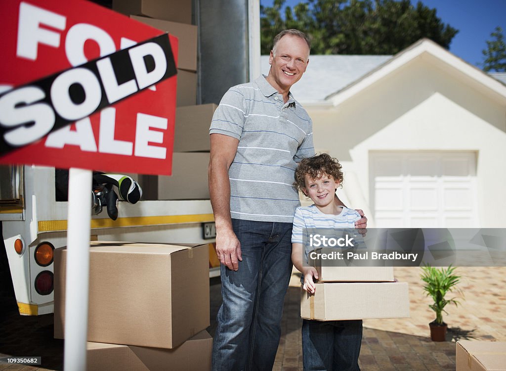 Padre e hijo con cajas de pie cerca de señal de venta - Foto de stock de Casa libre de derechos