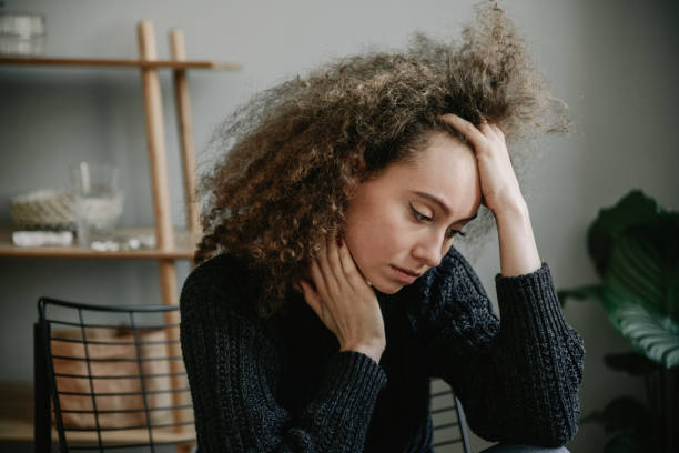 adolescente morena con depresión solo sentado en el sillón en la habitación gris. tristeza, nostlagic, depresión. problemas mentales de los jóvenes. - drug abuse addiction women violence fotografías e imágenes de stock