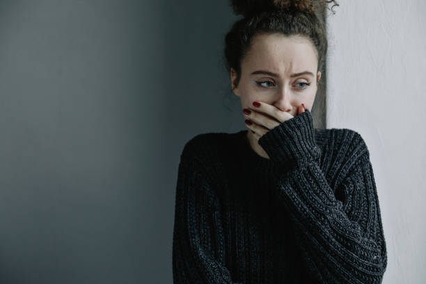 cerca de adolescente con depresión y bulimia sentado solo en el cuarto oscuro. ella cubre su rostro con las manos. problemas mentales con depresión y bulimia. - drug abuse addiction women violence fotografías e imágenes de stock