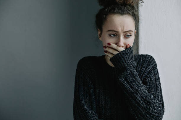 Close up of teenager with depression and bulimia sitting alone in dark room. She covers her face with hands. Mental problems with depression and bulimia. Mental problems of young people. Depression, bulimia, addicted. Social issue. phobia stock pictures, royalty-free photos & images