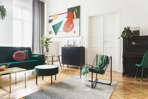 istock Sunny luxury home interior with design velvet sofa, armchair, tables, pouf, commode and accessroies. Nice plants on the piano. White walls with painting. Big windows. Stylish decor of sitting room. 1093510322