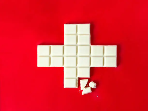 Photo of Swiss flag cross in form of white chocolate with some pieces over the red background
