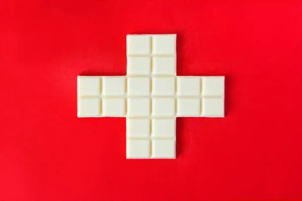 Photo of Swiss flag cross in form of white chocolate over the red background