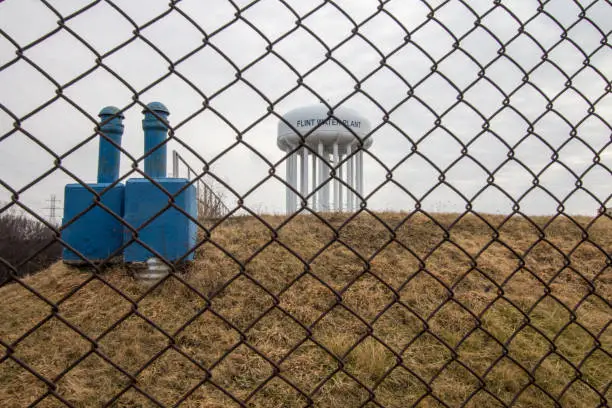 Water tower of Flint Michigan through a chain linked fence. The city came into the national spotlight during the Flint Water Crisis.