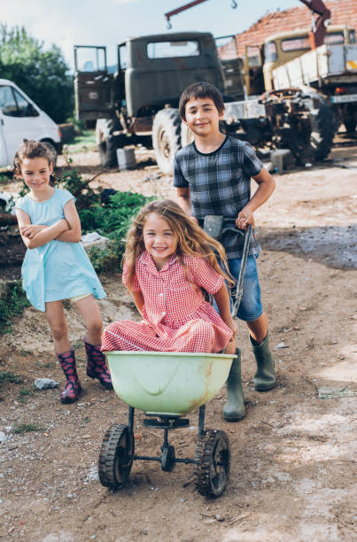 garota em um carrinho de mão - wheelbarrow playing sibling rural scene - fotografias e filmes do acervo