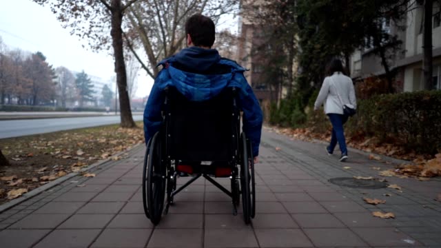 Young man riding in his wheelchair along sidewalk