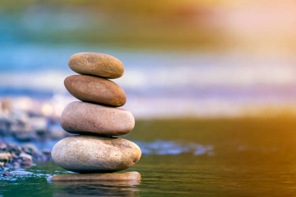 istock Close-up abstract image of wet rough natural brown uneven different sizes and forms stones balanced like pyramid pile landmark in shallow water on blurred blue-green misty copy space background. 1093531624