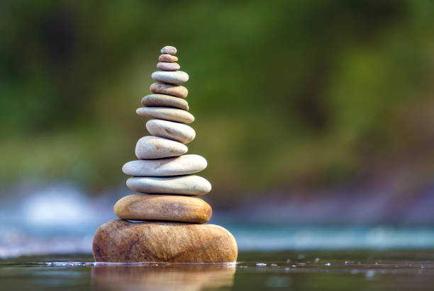 istock Close-up abstract image of wet rough natural brown uneven different sizes and forms stones balanced like pyramid pile landmark in shallow water on blurred blue-green misty copy space background. 1093544182