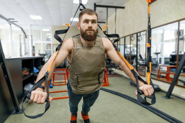 筋肉のひげを生やした男はジムでストラップ システムを使用しての演習を行う軍事加重装甲ベストに身を包んだ。スポーツ、トレーニング、ボディービル、健康的なライフ スタイルのコン� - protection life security train ストックフォトと画像