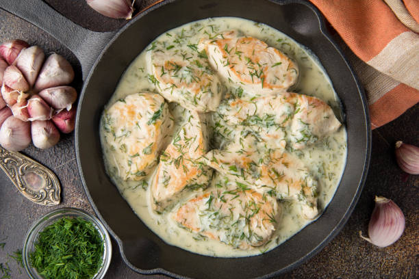 Chicken fillet or Turkey breast in creamy sauce with dill and garlic, in cast iron black pan on dark background. Delicious homemade food stock photo