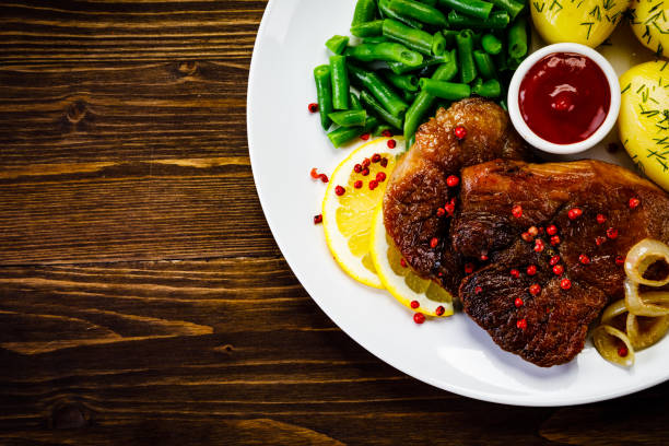 istock Grilled steak, boiled potatoes and vegetables on wooden background 1093570810