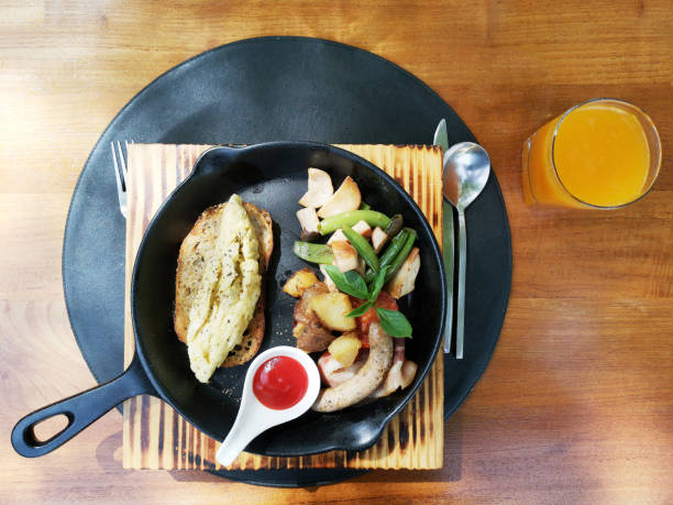 set de desayuno americano, tortilla, salchicha, tocino, tomate fresco y vegetal en la placa negra con tenedor cuchara y cuchillo en una mesa de madera se sirven con jugo de naranja. - omelet bacon tomato fruit fotografías e imágenes de stock