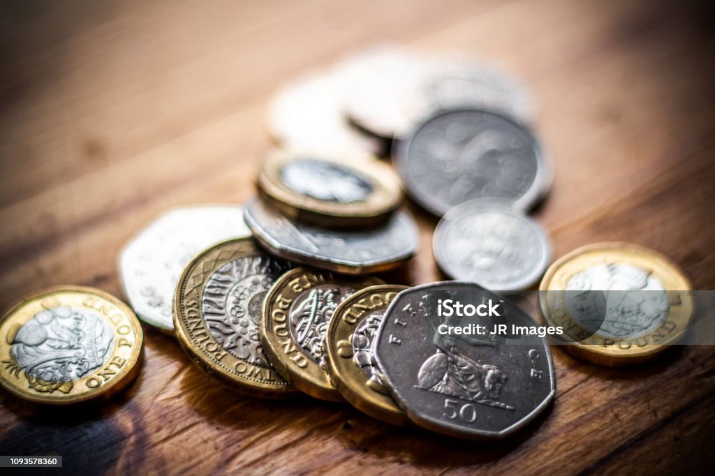 New Great British Pound GBP Coins laying casually on wooden surface. Wealth, Money, Cash, Change. British Currency, Coins on top of wallet. Currency Stock Photo