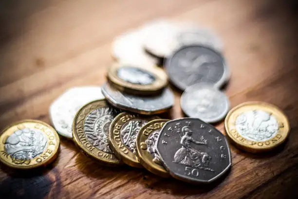 Photo of New Great British Pound GBP Coins laying casually on wooden surface. Wealth, Money, Cash, Change.