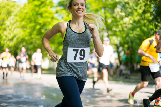 happy smiling young woman running marathon on sunny day in spring on street through park