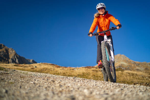 donna sorridente in bicicletta con mountain bike elettrica in montagna freddo ma soleggiato e cielo azzurro chiaro - european alps cold mountain range clear sky foto e immagini stock