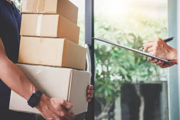 Home delivery service and working with service mind, Woman customer signing and receiving a cardboard boxes parcel from deliveryman.