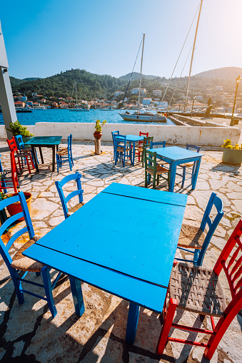 Colorful table and chairs in a typical tavern by the sea. Greek fishing village at hot summer day.