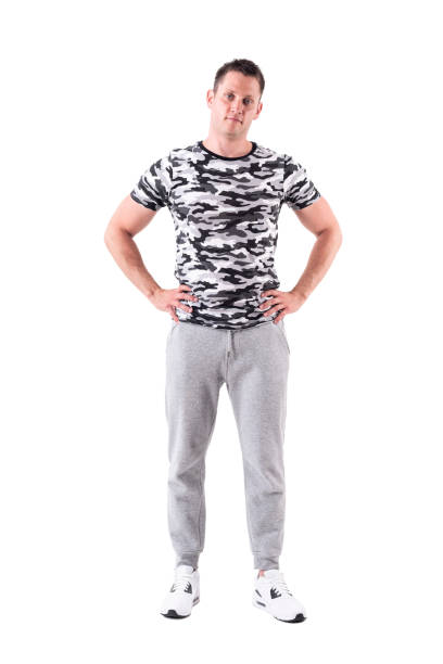 расслабленный молодой фитнес-модель позирует с руками на бедрах с взведенной головой - camouflage pants стоковые фото и изображения
