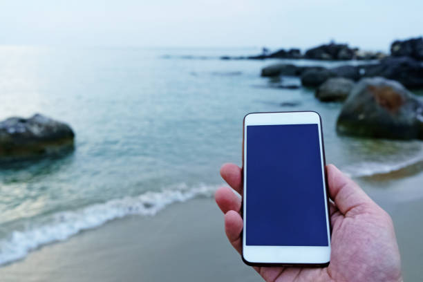 istock Smart phone in hand on the sea background. Mockup image 1093644082