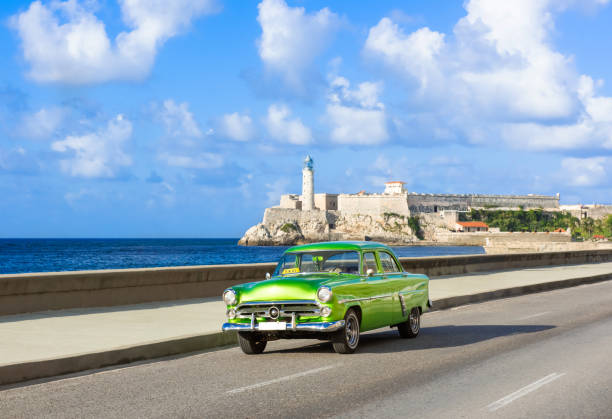 American green 1952 vintage car on the promenade Malecon and in the background the Castillo de los Tres Reyes del Morro in Havana City Cuba - Serie Cuba Reportage stock photo