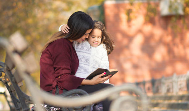 madre e figlia hanno letto la storia del libro sulla panchina del parco cittadino. - book child staircase steps foto e immagini stock