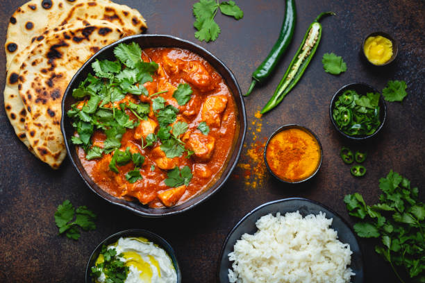 plat indien traditionnel poulet tikka masala avec curry épicé la viande dans le bol, riz basmati, pain naan, sauce raita yaourt sur fond foncé rustique, vue de dessus, se bouchent. dîner de style indien d’en haut - plat exotique photos et images de collection