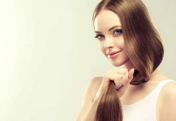 giovane modello bello dai capelli castani con capelli lunghi e dritti tiene la coda di capelli ben curati e sani nella mano. - capelli lisci foto e immagini stock