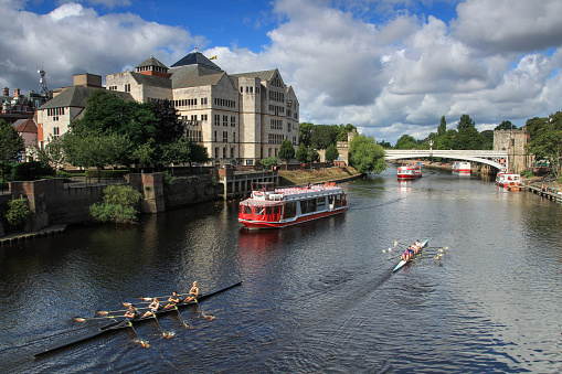 York, UK - September  2, 2015.  A river cruise boat and rowing club boats sailing along the River Ouse in the centre of the historic City of York, UK