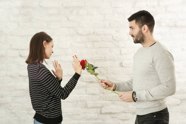 portrait of a young couple having conflict. man asking for forgiveness offering a red rose flower to his offended girlfriend - pleading men women reconciliation imagens e fotografias de stock