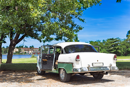 American green white classic car with open door parked under a tree on the beach in Varadero Cuba -Serie Cuba Reportage