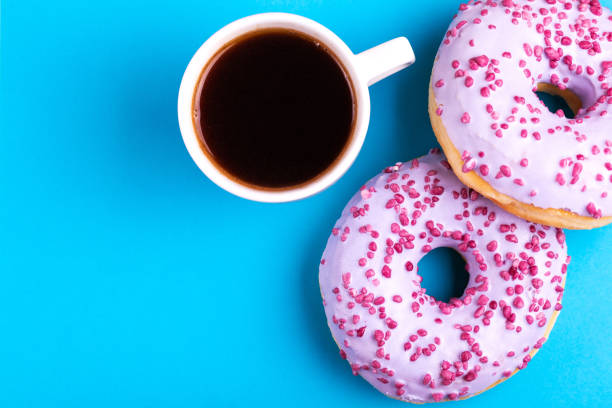 istock Two tasty lilac donuts with sprinkle and cup of strong coffee on bright blue background 1093672276