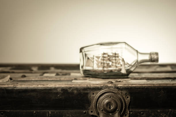 Ship in a small glass bottle sits in sand on empty beach