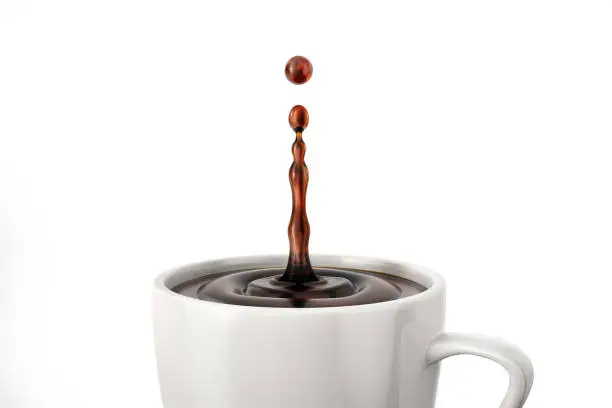 Photo of Single drop of coffee splashing into a white cup mug. Close up view.