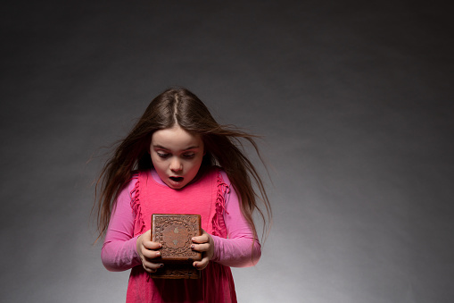 A little girl with a pink dress looks very astonished in a box