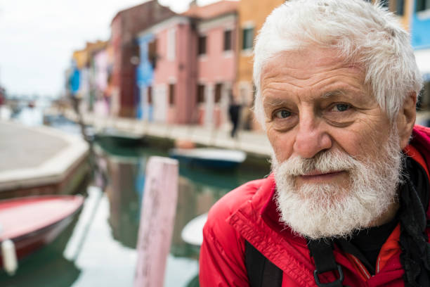 Portrait of senior man against canal and colorful facades of old village on island Burano.