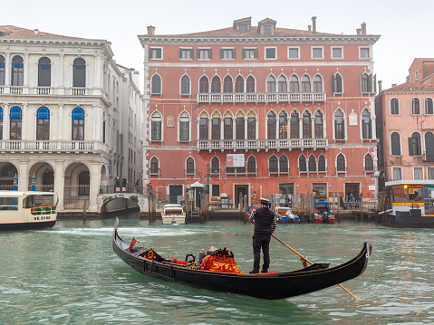 Venice, Italy - December 21, 2018: Gondolier standing up Gondola and rowing one oar through the Grand Canal at foggy winter day