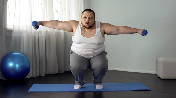 istock Overweight man squatting and lifting dumbbells on mat, full body training home 1093734432