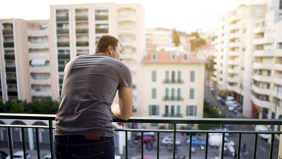 Man enjoying view from his hotel suite balcony on busy street, business trip