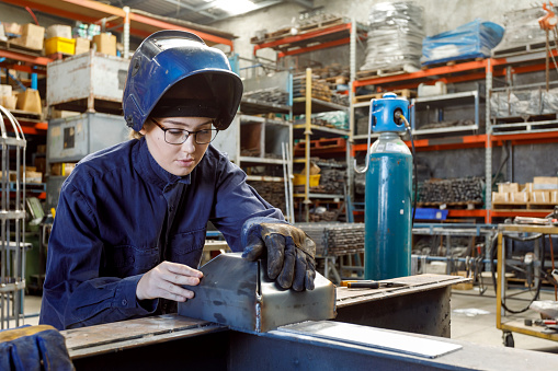 Young Female Welder Inspecting Her Work In Factory Wearing Protective Safety Gear