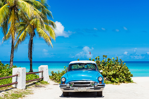 Coche clásico azul americano con un techo blanco estacionado debajo de las palmas directo en la playa en Varadero Cuba - Serie Cuba reportaje photo