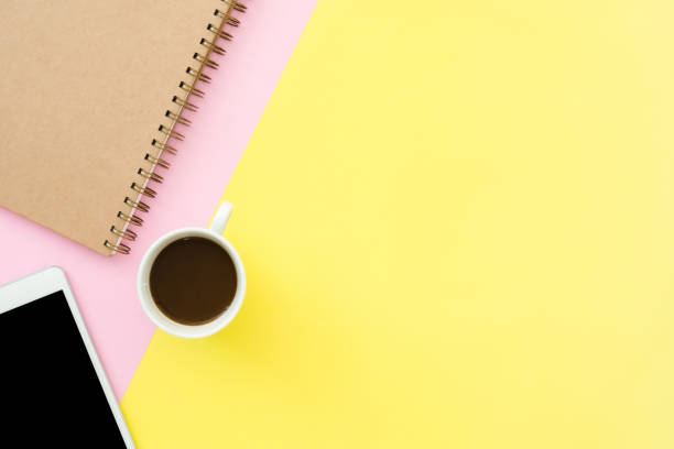 istock Office desk working space - Flat lay top view photo of working space with blank mock up tablet, coffee cup and notebook on pastel background. Pastel pink yellow color copy space working desk concept. 1093762340