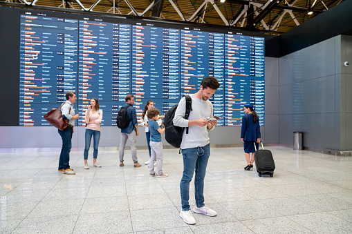 People traveling and looking at the flight schedule at the airport - travel concepts
